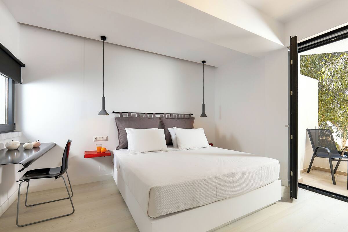 Un dormitorio moderno con una cama grande, un escritorio con una silla y un balcón con una silla.