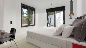 Quarto moderno com uma cama grande, uma escrivaninha e uma cadeira. Possui duas janelas e uma porta que dá para uma área externa.