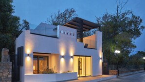 Uma casa moderna de dois andares, com varanda, grandes janelas e uma entrada bem iluminada.