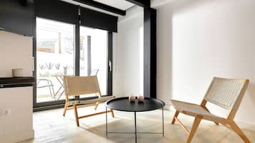 Un interior moderno con una mesa redonda negra, dos sillas de mimbre y un amplio ventanal con vistas al exterior.