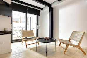 Un intérieur moderne avec une table ronde noire, deux chaises en osier et une grande fenêtre donnant sur l’extérieur.