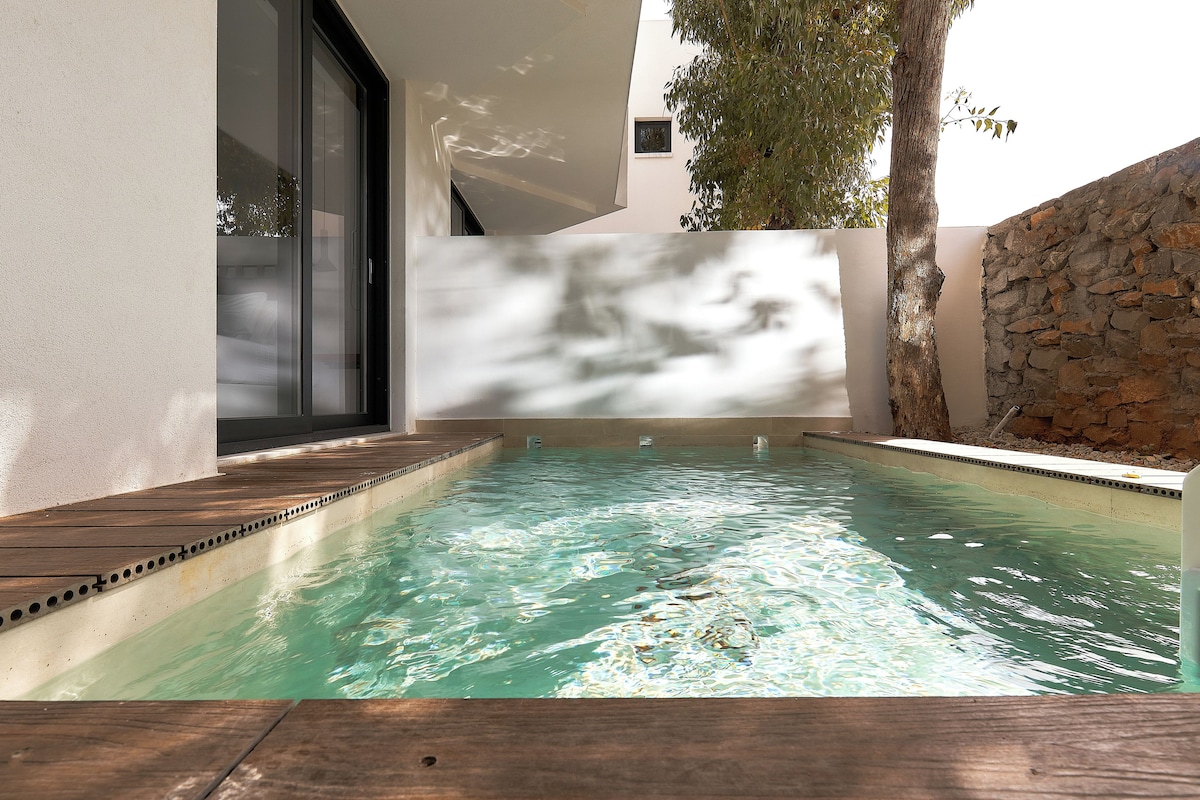 Une piscine avec une terrasse en bois, un mur en pierre et une porte en verre.