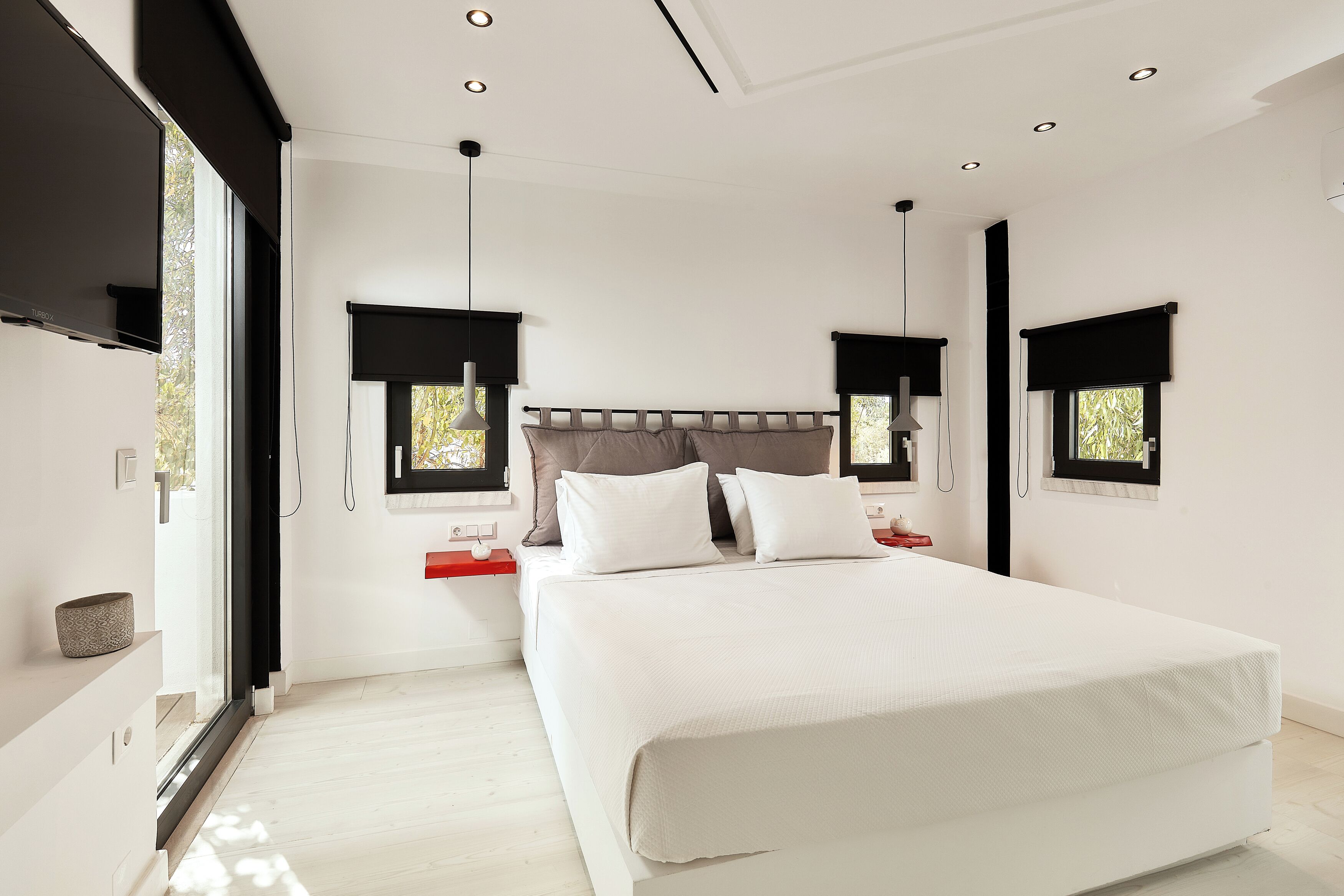 A modern bedroom with a large bed, two bedside tables, and a TV mounted on the wall.