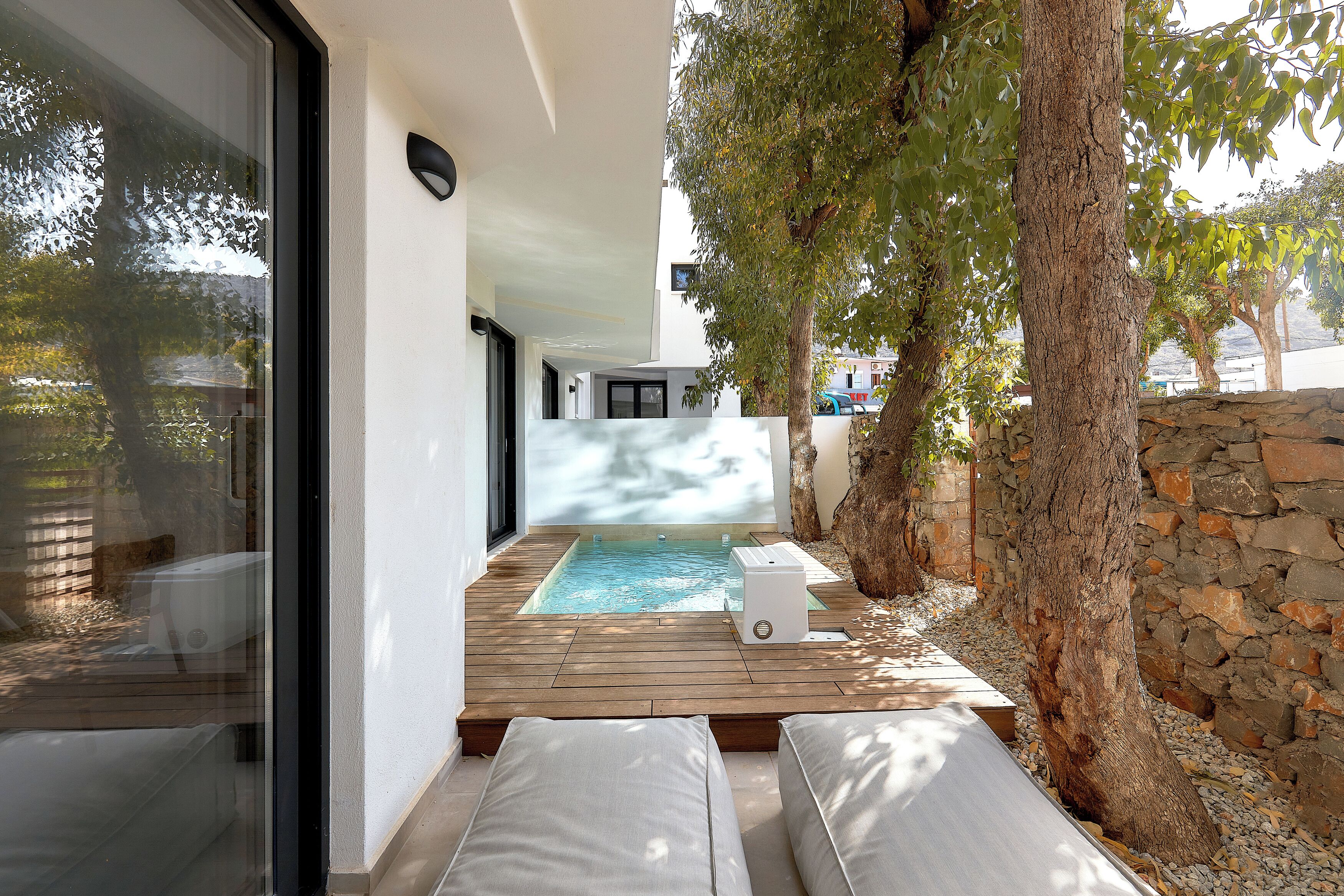 A modern outdoor pool area with wooden decking, a built-in hot tub, and a stone wall.
