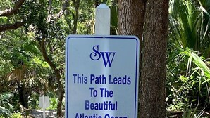 A signpost with the text "This Path Leads To The Beautiful Atlantic Ocean" and a compass arrow indicating the direction.