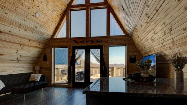 Een gezellig cabin interieur met een hoge plafond, een groot raam en een bordje met de tekst 'This must be the place'.