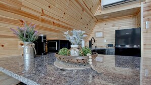 Een keuken met houten wanden, granieten aanrecht, een koffiezetapparaat, een koelkast en een decoratieve plantencompositie.