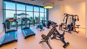 Une salle de sport équipée de tapis de course, d’un appareil elliptique et de machines de musculation, avec de grandes fenêtres donnant sur l’extérieur.