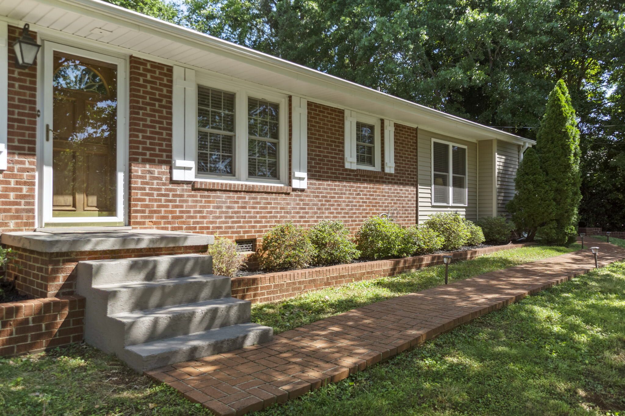 A two-story brick house with a front porch, a set of concrete steps, and a brick pathway leading to the front door.