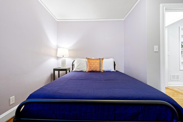 Un dormitorio con cama, mesita de noche, lámpara y puerta que da a otra habitación.