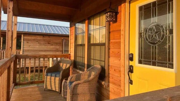 A wooden porch with wicker chairs and a yellow door with a star emblem.