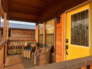 A wooden porch with wicker chairs and a yellow door with a star emblem.