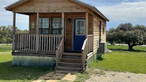 Une cabane en bois avec une véranda, une porte bleue et un petit escalier menant à l’entrée.