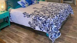Une chambre à coucher comprenant un lit, un ventilateur de plafond, une table de chevet, une commode, un miroir et des tableaux encadrés accrochés au mur.