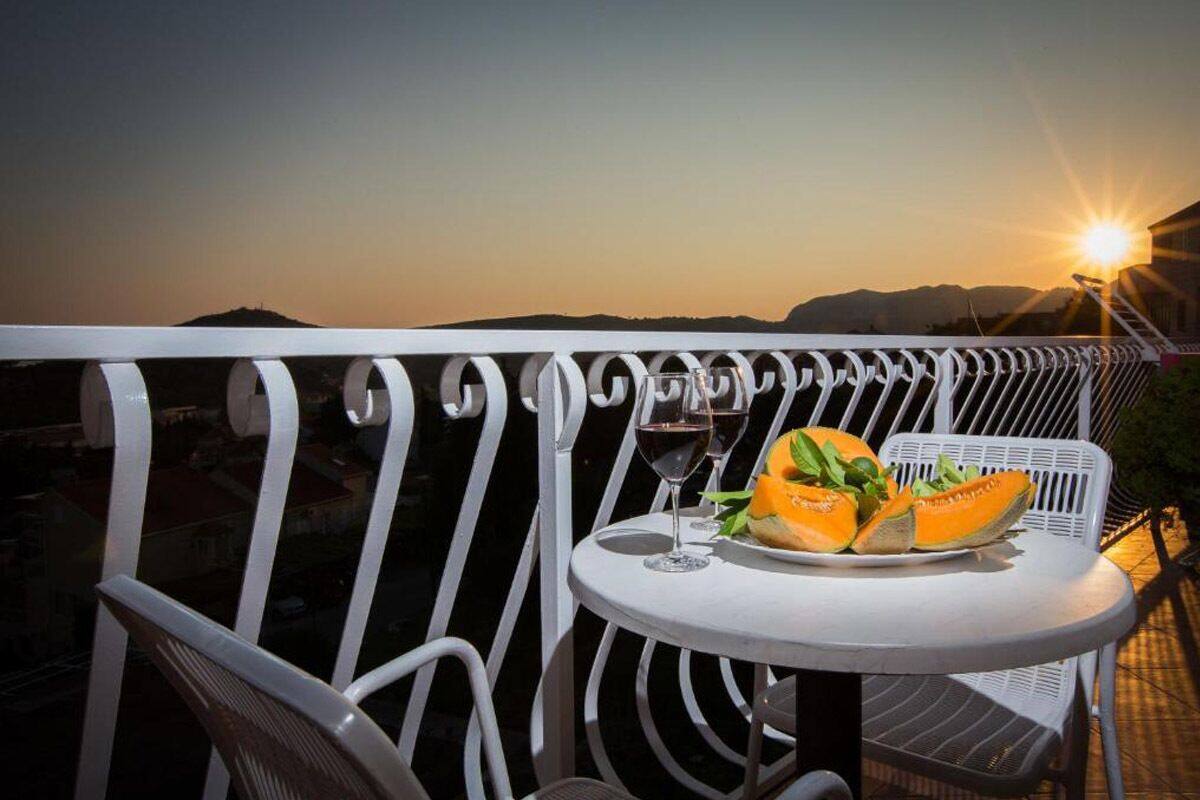 A balcony with a table set for two, featuring a plate of sliced fruit and two wine glasses.