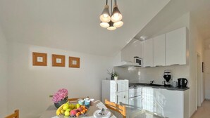 Een moderne keuken met witte kasten, een eettafel met een fruitschaal en een hanglamp.