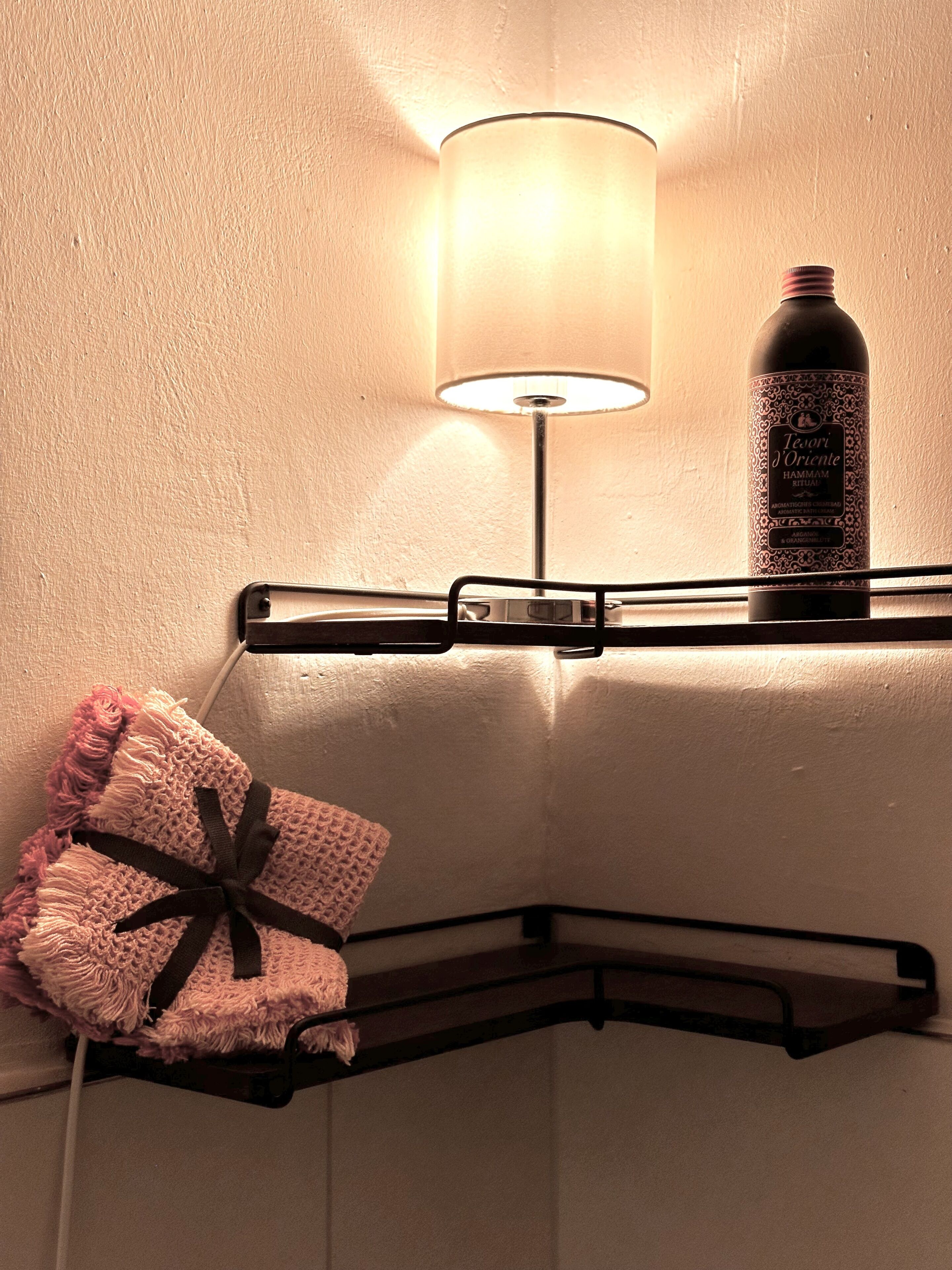 A bathroom shelf with a bottle of shampoo, a towel, and a lamp.