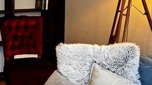 Une pièce avec un fauteuil rouge, une lampe sur un trépied et une bibliothèque avec une bougie.