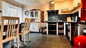 Une cuisine de taille réduite, avec des carreaux de couleur sombre, des chaises en bois, une table à manger et un appareil électroménager rouge.