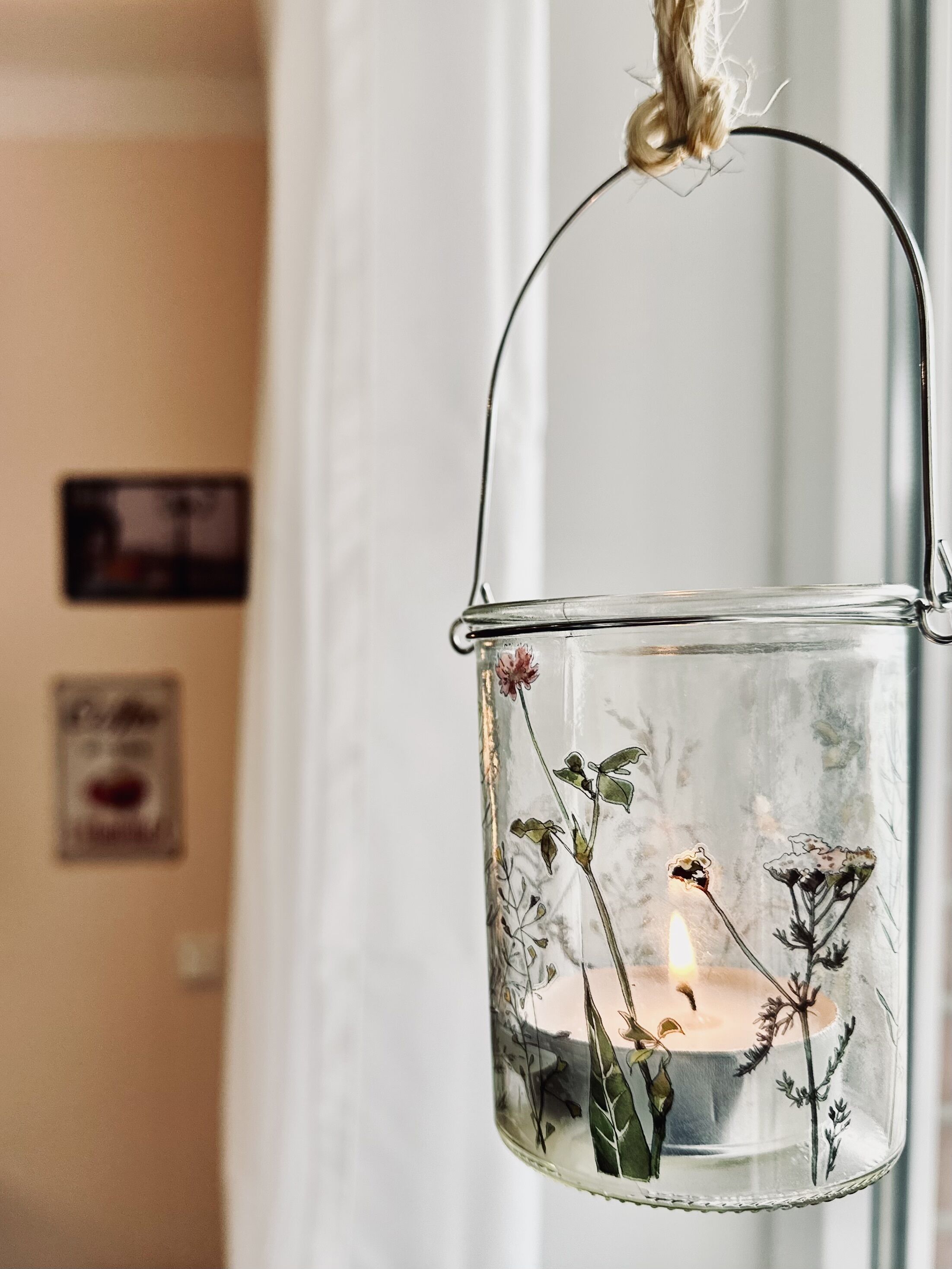 Llanterna de vidre transparent amb motius florals i una espelma a l'interior, penjada d'una corda.
