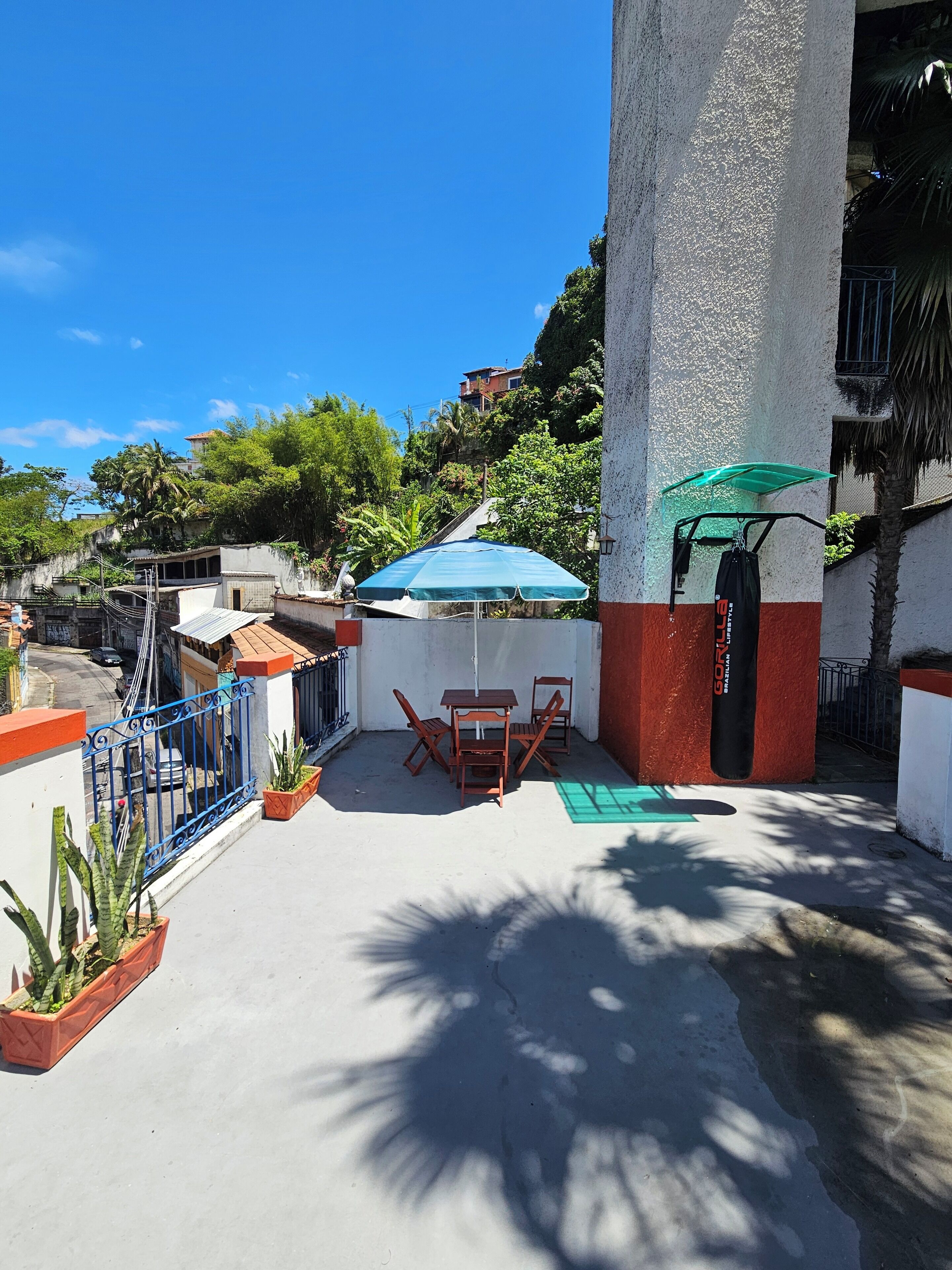 An outdoor patio area with a table and chairs, a green umbrella, and potted plants.