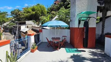 An outdoor patio area with a table and chairs, a green umbrella, and potted plants.