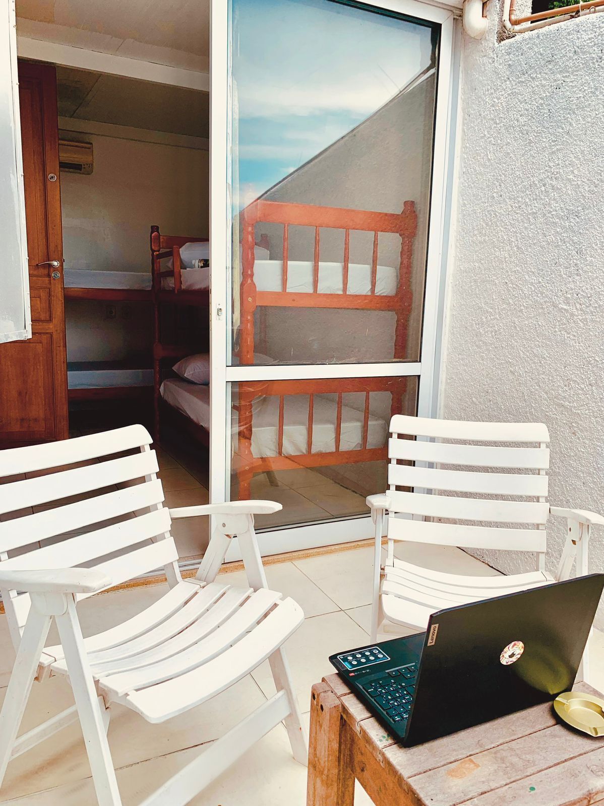 A balcony with two white chairs, a laptop on a small table, and a wooden bench.