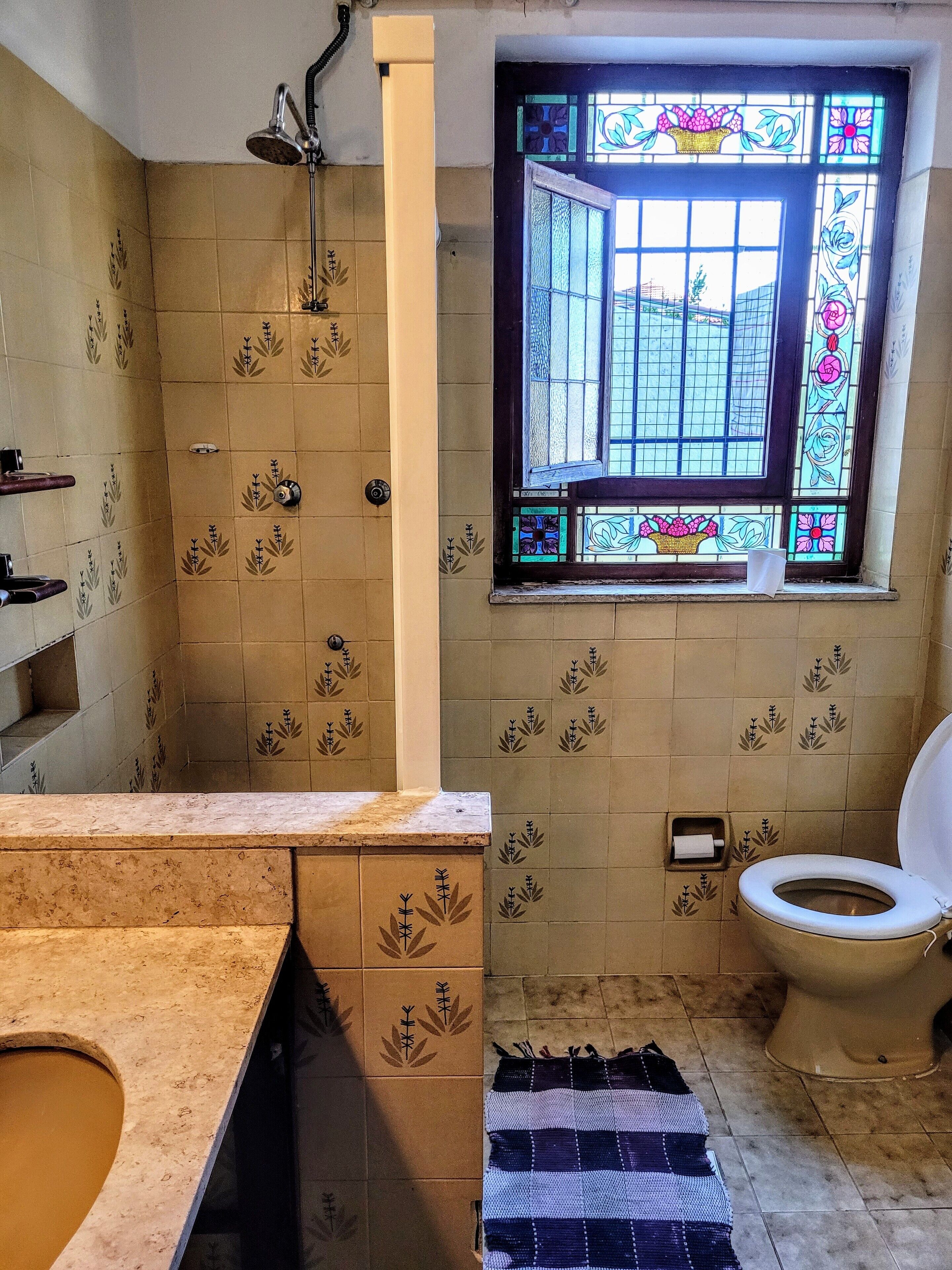 Une salle de bain avec douche, toilettes et une fenêtre ornée de vitraux.
