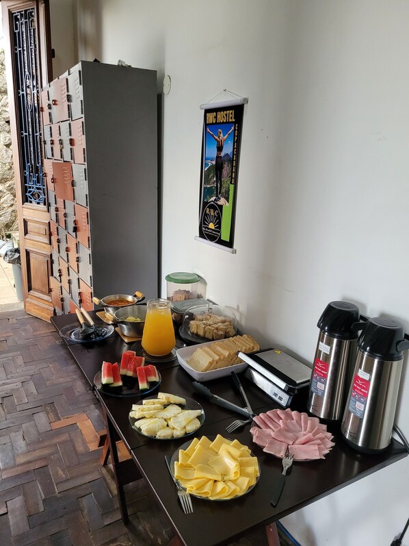Um buffet de café da manhã com diversos alimentos, um cartaz na parede e um dispensador de água.