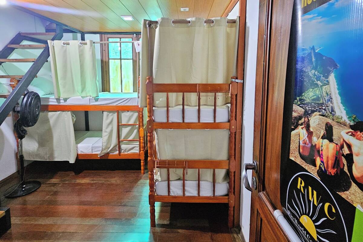 A hostel room with bunk beds, a wooden staircase, and a poster advertising the hostel.