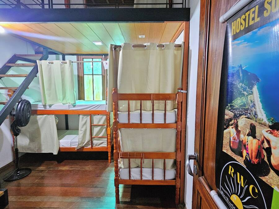 Habitación de hostal con literas, una escalera de madera y un cartel publicitario del hostal.