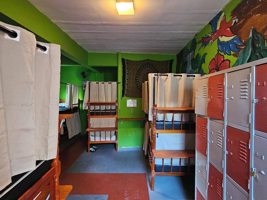 Une chambre de dortoir avec des lits superposés, un ventilateur et des casiers.