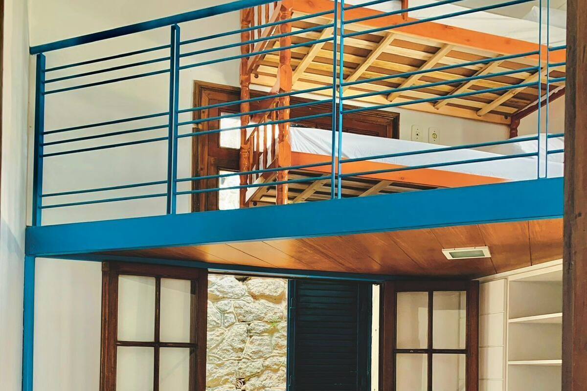A bunk bed room with a wooden headboard, a window with a stone wall outside, and a blue railing on the upper bunk.