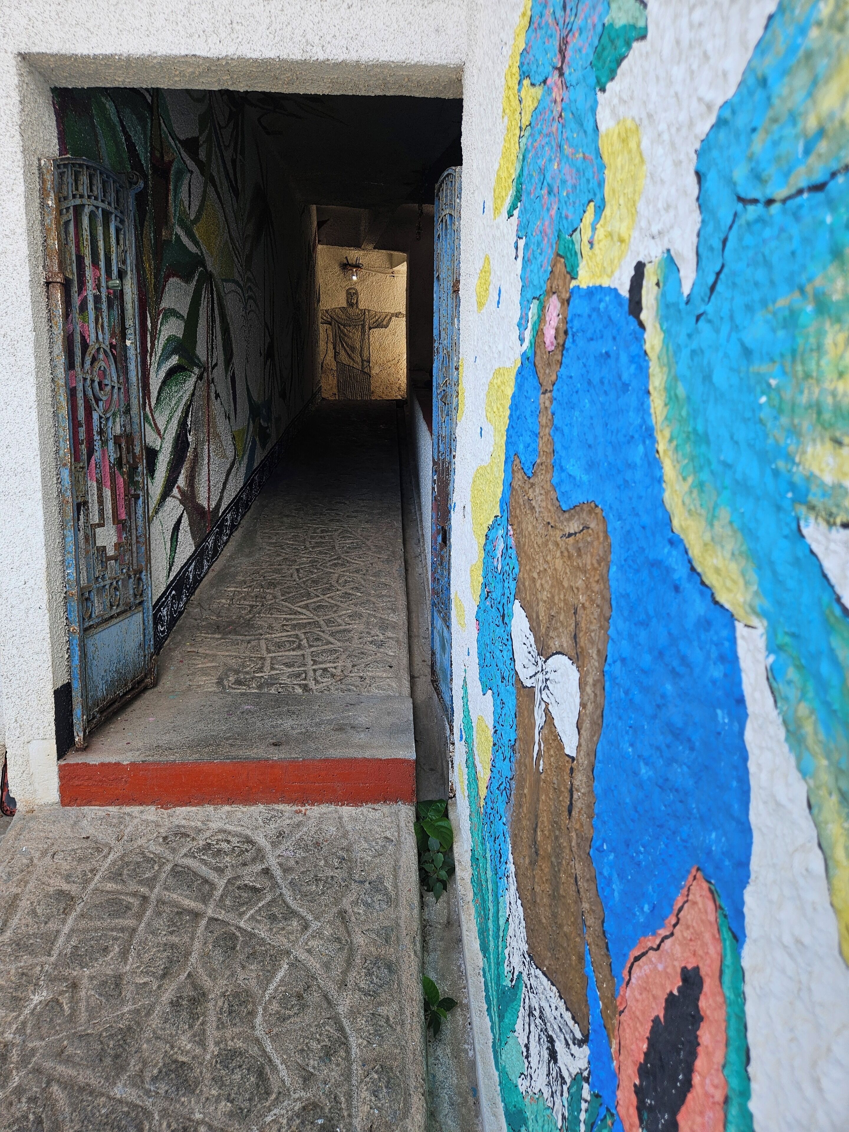 Un couloir étroit, doté d’un sol à motifs et d’une fresque sur le mur de droite.