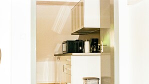 Een compacte kitchenette met een magnetron, koffiezetapparaat en broodrooster. Er is een prullenbak en een kast met lades.