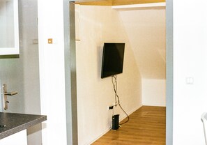 Ein Zimmer mit Holzboden, weißer Wand und einem an der Wand befestigten Flachbildfernseher.