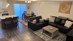A modern living room with a black leather sofa, wooden coffee table, and a dining area with a wooden table and chairs. - New 2 BR Townhouse in the Heart of Wenatchee. Great for Families, pet friendly. (Wenatchee)