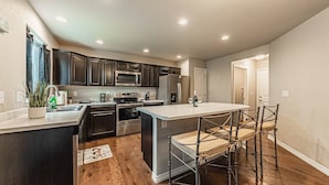A modern kitchen with dark wood cabinets, stainless steel appliances, and a central island with bar stools. - •Lamine Elegance Drive• FreeWine, GameRoom & HotTub (Colorado Springs)