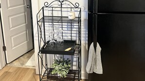 Une cuisine avec un réfrigérateur noir, un meuble à bouteilles de vin, un panneau décoratif sur le thème du café et une plante en pot.