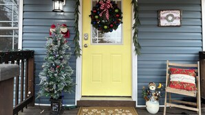 Une porte jaune ornée d’une guirlande, un sapin de Noël et un paillasson.