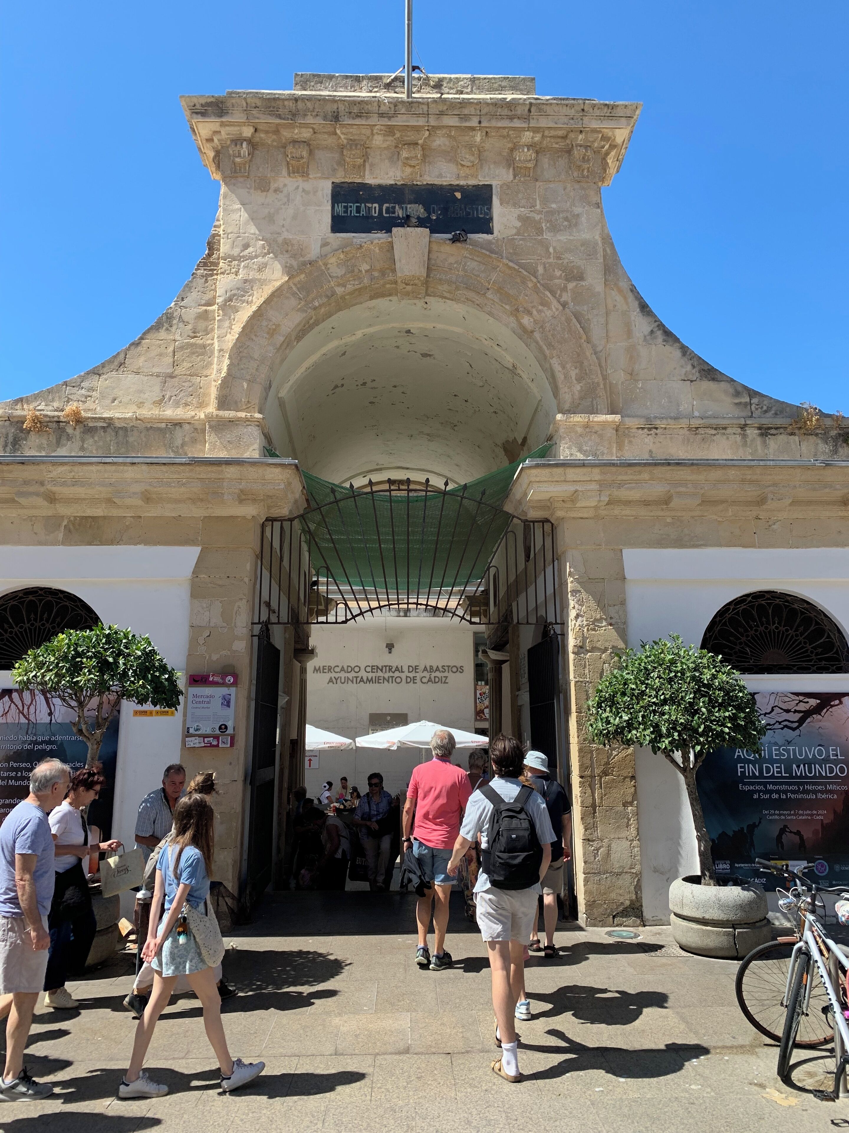 An entrance to a historic building with a stone archway and a sign reading "Mercado Central de Abastos Ayuntamiento de Cádiz".