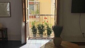 Una stanza con un tavolino in legno, una pianta in vaso e vista su un balcone con piante e ringhiera.