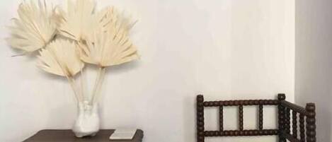 A room with a dark wooden chair, a small table with a white vase containing dried flowers, and a round mirror on the wall.