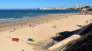 Una spiaggia con persone, cielo sereno e edifici in lontananza.