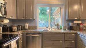 A modern kitchen with granite countertops, stainless steel appliances, and a window offering a view of greenery. - Cozy 5BR Ranch Home with Hot Tub in Quiet Folsom Neighborhood (Folsom)