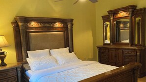 A bedroom with a large bed, wooden headboard, a nightstand with a lamp, and a dresser with a mirror. - Cozy 5BR Ranch Home with Hot Tub in Quiet Folsom Neighborhood (Folsom)
