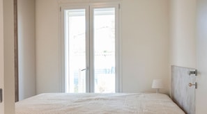 A bedroom with a bed, a nightstand, a lamp, and a window with a view of the outside.
