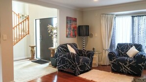 A living room with two patterned armchairs, a side table, a floor lamp, and a large window with curtains. - Luxury Large 2 Storied Villa Walk to Shopping Mall Howick (Auckland)