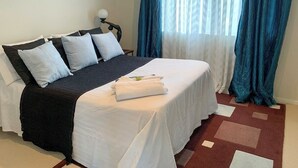 A neatly made bed with white and dark bedding, a lamp, and a window with blue curtains. - Luxury Large 2 Storied Villa Walk to Shopping Mall Howick (Auckland)
