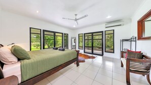 A bedroom with a bed, a chair, and large windows. - Riverside Homestead (Darwin River)